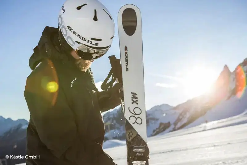 Esquiador sujetando su equipo con el sol de fondo