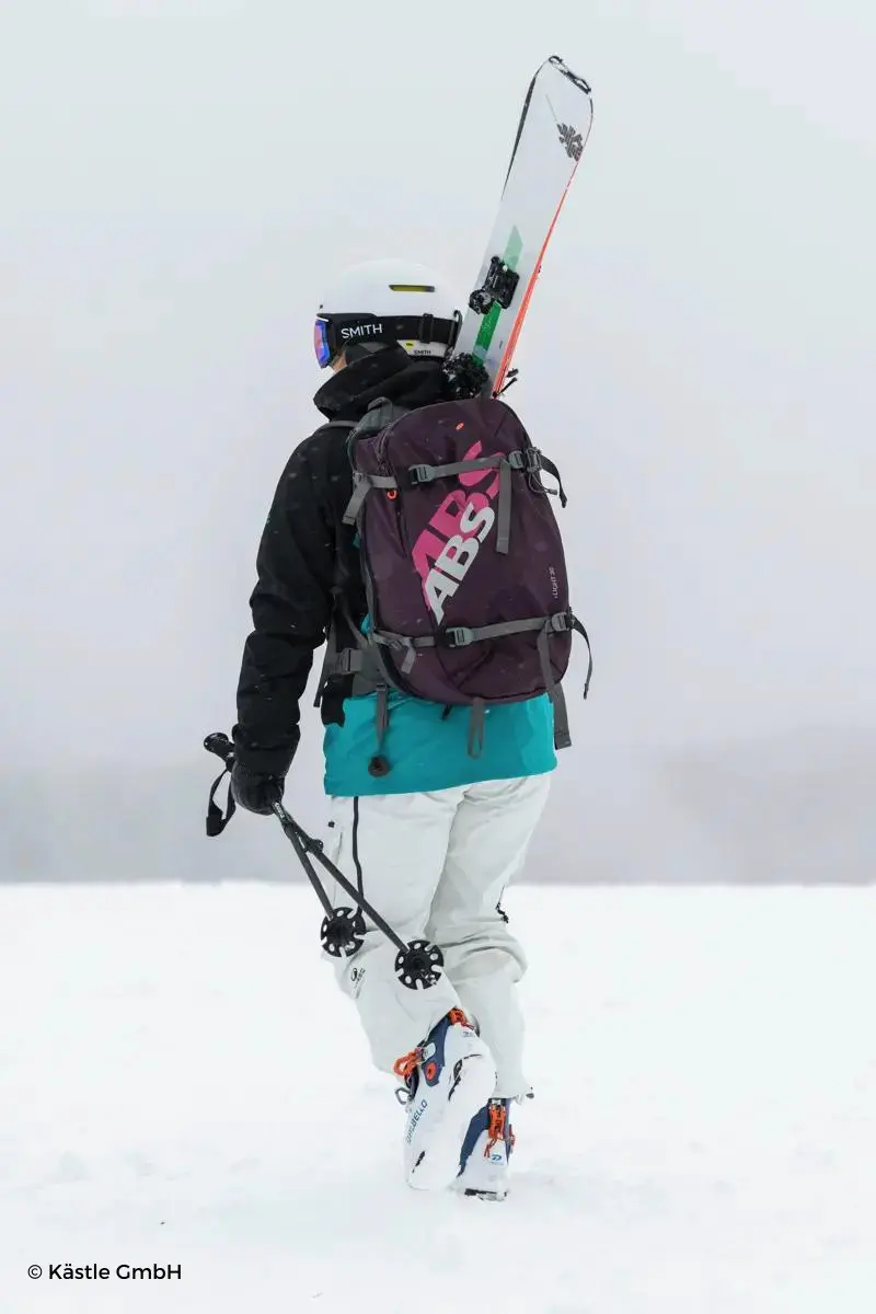Esquiador de espaldas portando su equipo