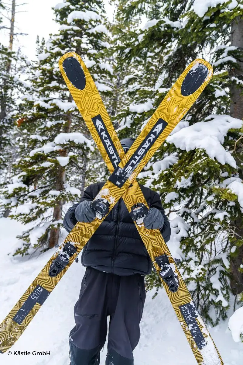 Persona sujetando esquís amarillos de Kastle con árboles de fondo